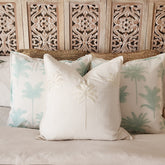 Decorative pillows with palm tree patterns on a bed with an ornate headboard.